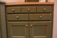 Thumb kitchen  traditional style  knotty alder  green painted with sand through and distress  recessed panel doors  2 rows of drawers over doors  baking center  butcher block top  3 top drawers  standard overlay